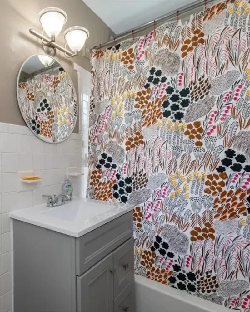 Bathroom before the design transformation, with a patterned shower curtain and exposed unfinished wall plate