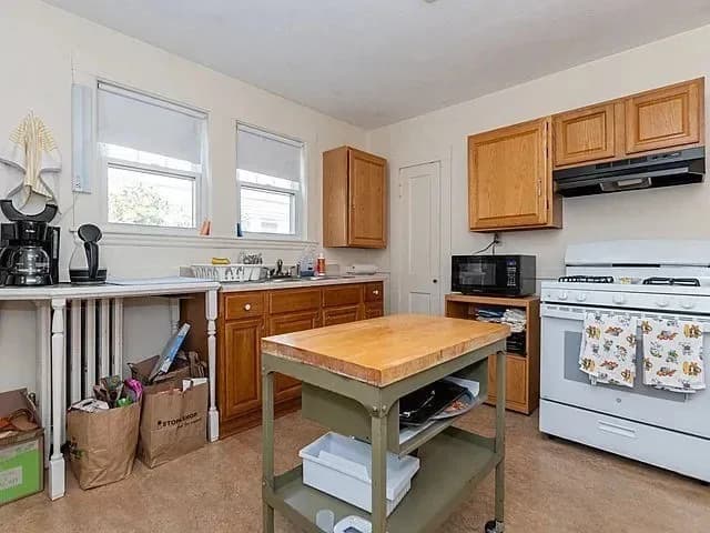 Kitchen before the design transformation, with mixed wood cabinetry and a freestanding work table
